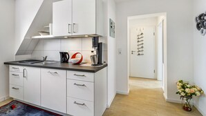 A modern kitchen with white cabinets, a black countertop, and a coffee machine. There is a door leading to another room and a vase with flowers on the floor. - Modern Apartment – Quiet & Prime Location in Neheim (Arnsberg)