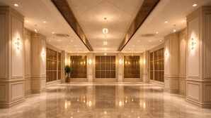 Un amplio vestíbulo de hotel con piso de mármol pulido, ventanas grandes con paneles de vidrio decorativos e iluminación ambiental proveniente de apliques de pared.