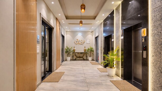 Un vestíbulo de hotel con piso de mármol, mostrador de recepción, plantas en macetas y un moderno ascensor.