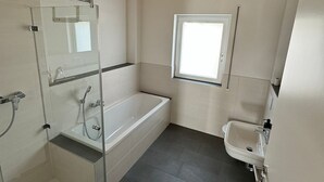Ein modernes Badezimmer mit Duschkabine aus Glas, einer Badewanne, einem Fenster und einem Waschbecken.