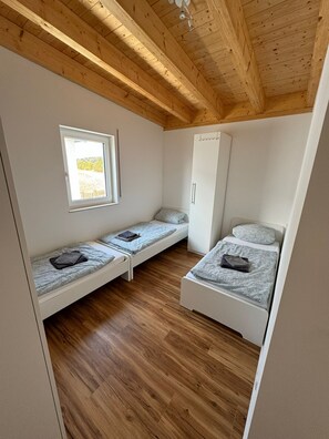 Une petite pièce comprenant deux lits superposés, une armoire, une fenêtre et un plancher en bois.