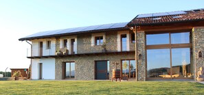Una casa de dues plantes amb façana de pedra, grans finestres i un balcó.