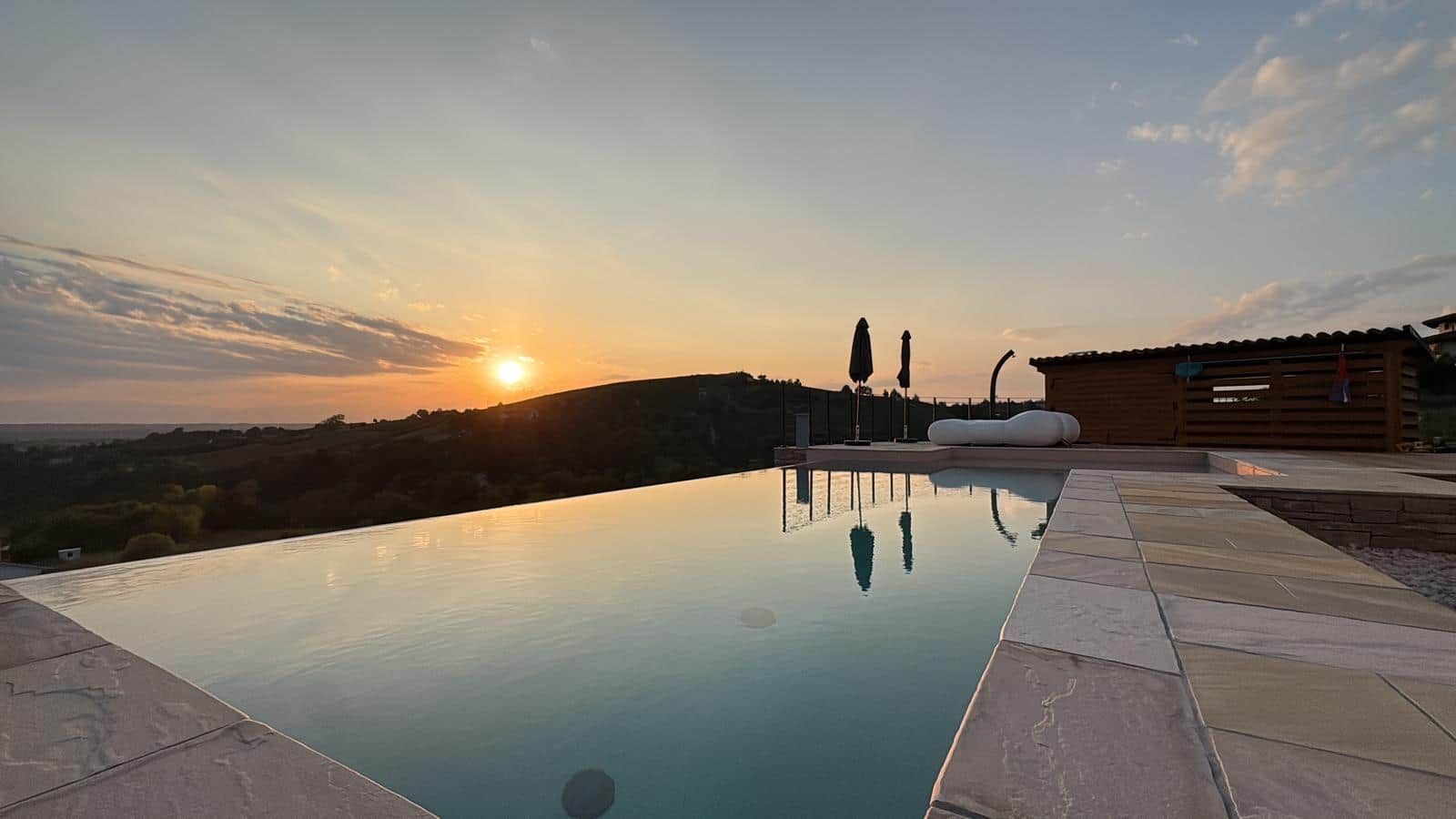 Ein Pool mit Sonnenuntergangsblick, eine Holzterrasse und ein modernes Gebäude im Hintergrund.