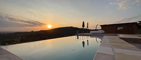 Una piscina con vista al atardecer, una terraza de madera y un edificio moderno al fondo.