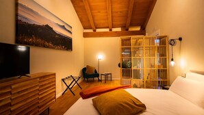 A bedroom with a bed, a TV, a wooden dresser, a chair, a small table, and a bookshelf. - Junior Suite with SPA & Pool (Dogliani)