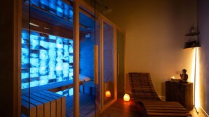 A sauna room with a glass partition, wooden benches, and a lit candle. - Junior Suite with SPA & Pool (Dogliani)