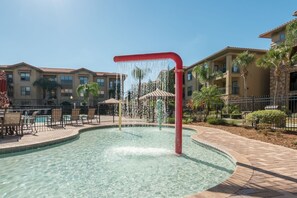 Une piscine agrémentée d’un élément décoratif aquatique, entourée d’un espace de détente extérieur et d’une clôture.