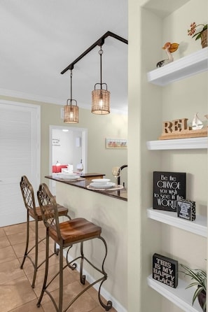Une cuisine avec un tabouret de bar, des luminaires suspendus et des objets décoratifs disposés sur des étagères.
