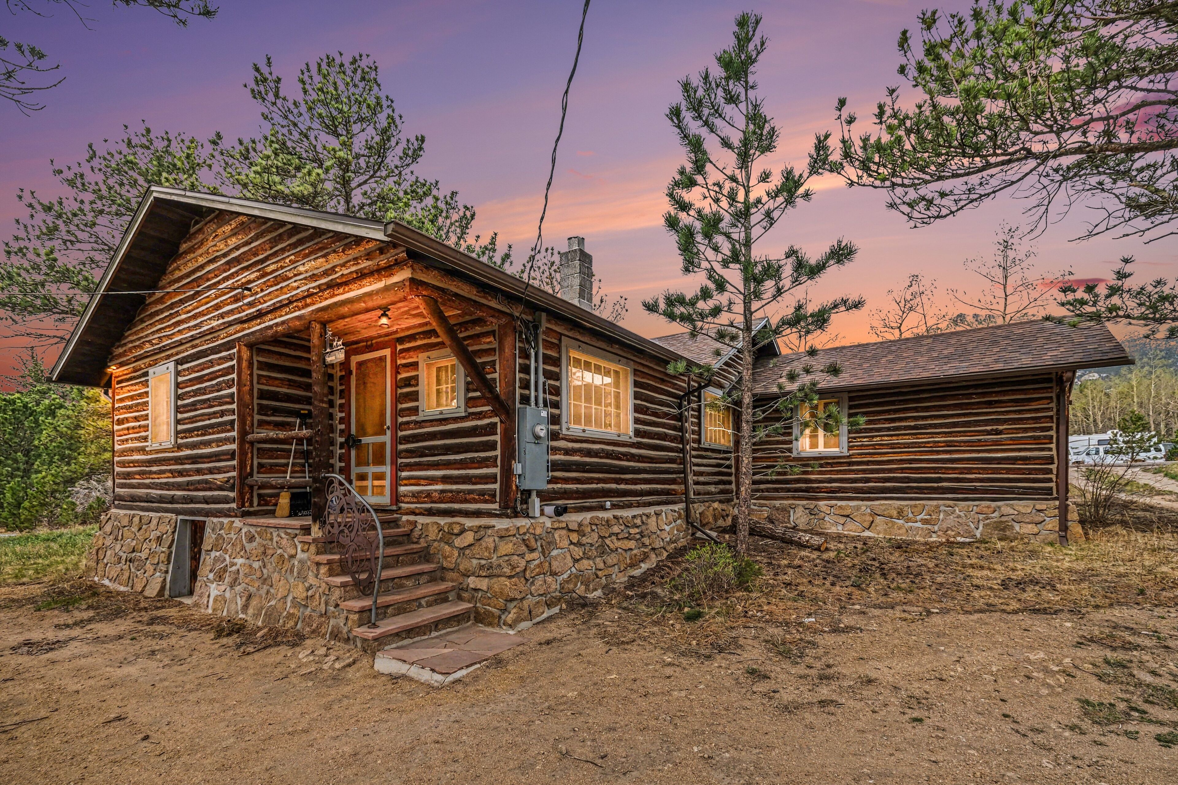 Une cabane en rondins avec des fondations en pierre, une véranda en bois et une cheminée.