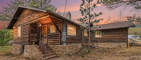 A log cabin with a stone foundation, a wooden porch, and a chimney.