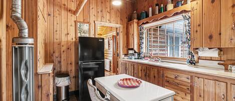 A wooden cabin interior with a kitchen area, including a refrigerator, stove, and dining table.