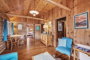 A log cabin interior with a dining area, a sofa, a cabinet, and framed pictures on the walls. - Thunderbird - Vr-24-0020 2 Bedroom Cabin (Allenspark)