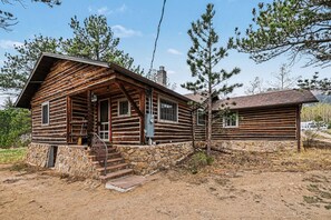 A log cabin with a stone foundation, a front porch, and a chimney. - Thunderbird - Vr-24-0020 2 Bedroom Cabin (Allenspark)