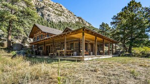 A log cabin with a porch, surrounded by trees and a mountain backdrop. - Historical Crocker Ranch - Rowe House 23-zone3423 3 Bedroom Home (Drake)