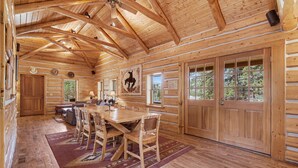 A log cabin interior with a wooden dining table, chairs, a rug, and large windows. - Historical Crocker Ranch - Rowe House 23-zone3423 3 Bedroom Home (Drake)