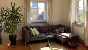 Ein Wohnzimmer mit einer Couch, einem Couchtisch, einer Zimmerpflanze und einem Fenster mit Vorhängen.