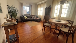 Ein Wohnzimmer mit einer Couch, einem Esstisch mit Stühlen, einer Holzkommode und einem Blumentopf.