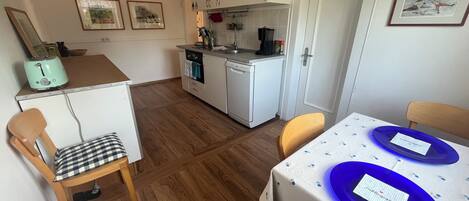 A compact kitchen with a toaster, oven, and sink. There are two chairs and a table with blue plates.