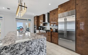 A modern kitchen with a marble island, stainless steel appliances, and wooden cabinetry. - Sophisticated 5 BR, Bikes, & Private Beach Access + Under New Management (Santa Rosa Beach)