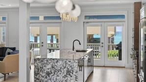Eine moderne Küche mit einer Marmorinsel, Doppeltüren, die auf einen Balkon führen, und Blick aufs Meer.