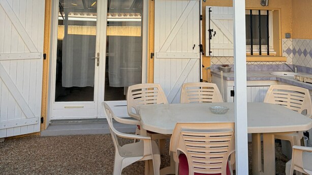 A covered outdoor patio with a table and chairs, a sliding glass door, and a tiled backsplash visible through the door.