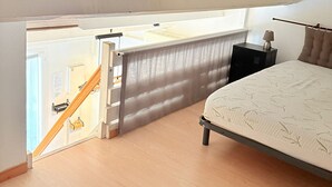 A bedroom with a bed, a nightstand, a lamp, a window, and a door.