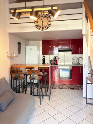 A kitchen with red cabinets, a wooden bar counter, and a clock. There is a dining area with a sofa and chairs.