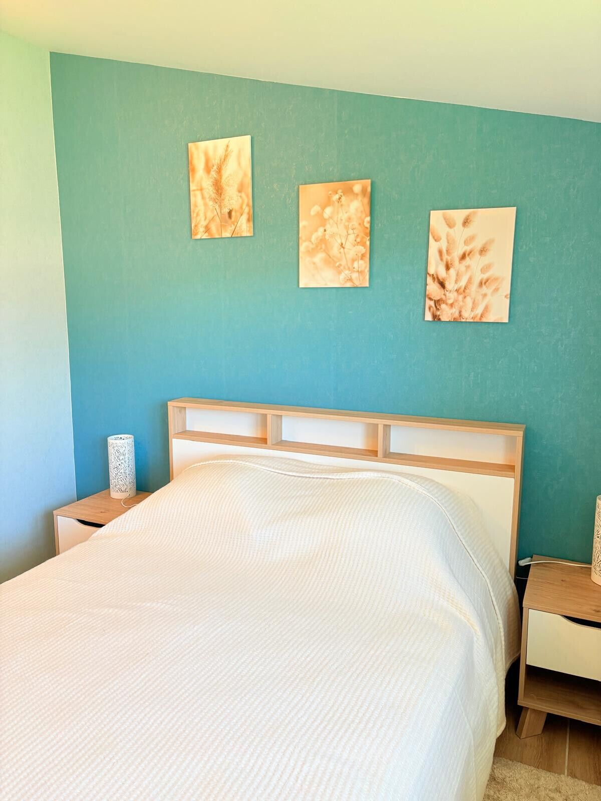 A bedroom with a bed, wooden headboard, and three wall-mounted artworks.