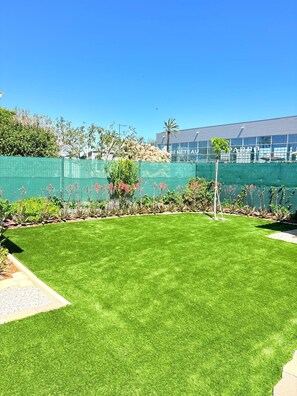 A well-maintained lawn with a green fence, a palm tree, and a building with 'BENETEAU' visible in the background. - St Cyprien, charming house and beautiful sunny exterior (Saint-Cyprien)
