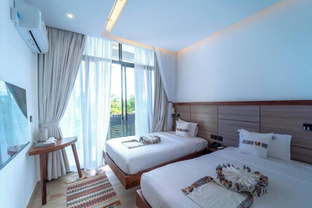 Habitación de hotel con dos camas, un escritorio, un equipo de aire acondicionado y vistas a zonas verdes.