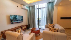 Una sala de estar moderna con un televisor de pantalla plana, dos sofás, una mesa de centro y un ventanal con cortinas.