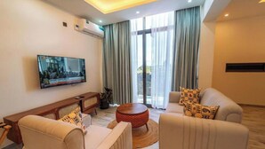 A modern living room with a flat-screen TV, two sofas, a coffee table, and a large window with curtains.