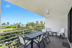 A balcony with a table and chairs, overlooking a beach and palm trees. - Beachview 2/2 condo, Pool, Beach (Longboat Key)