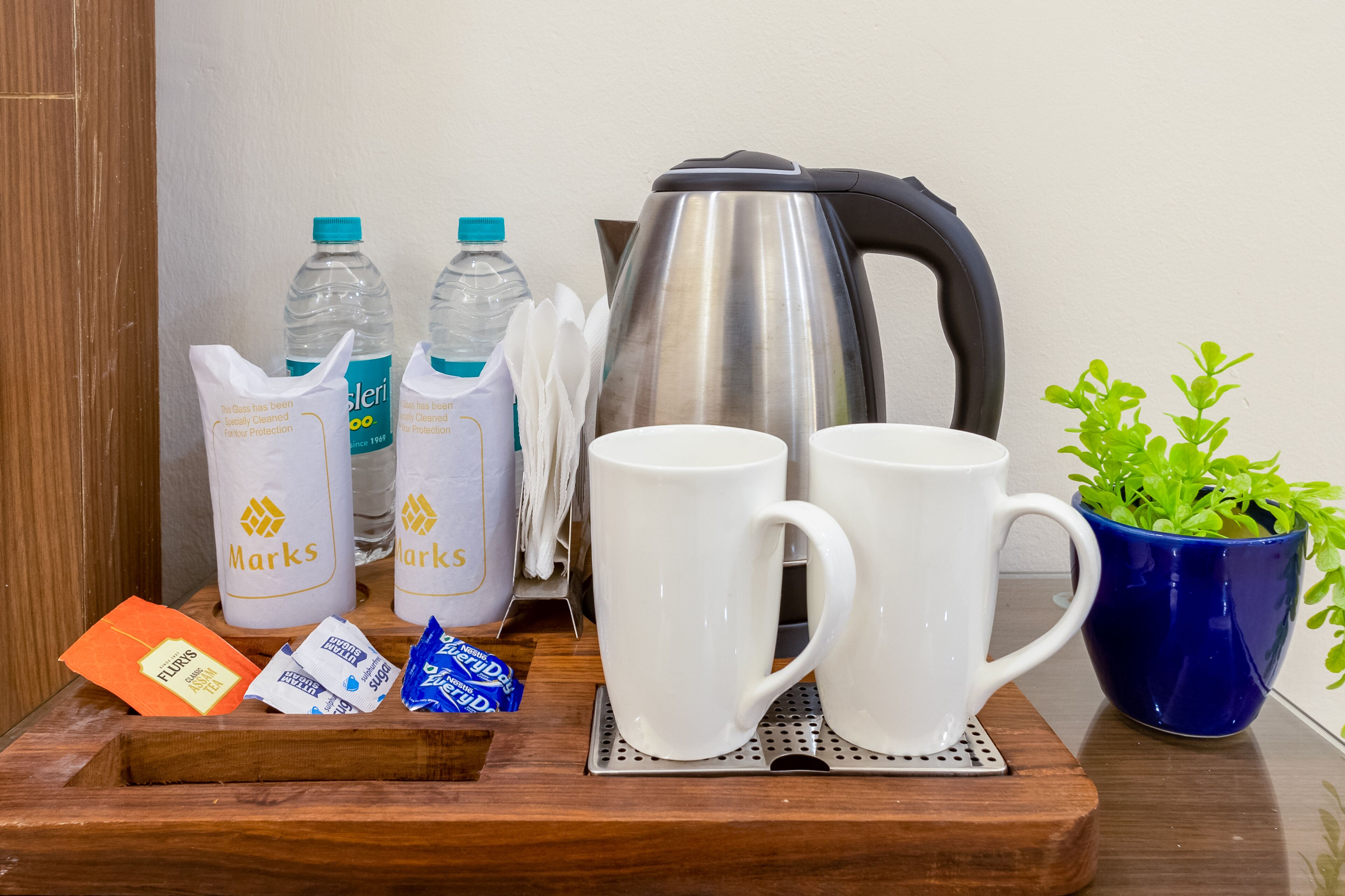 A tray with coffee mugs, a kettle, water bottles, and sugar packets.