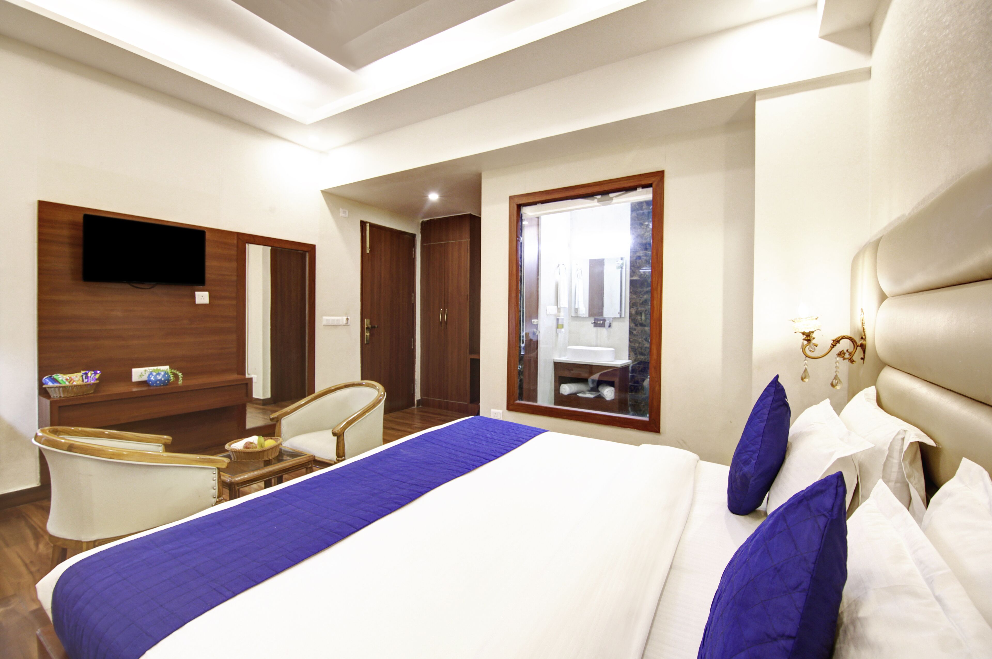 A hotel room with a bed, a television, a bathroom with a mirror, and a seating area with a chair.