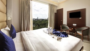 A hotel room with a bed, a desk, a chair, a television, and a view of the city.