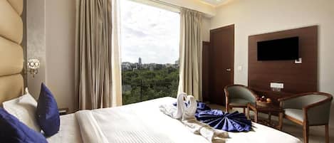 A hotel room with a bed, a desk, a chair, a television, and a view of the city.