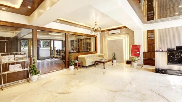 A spacious lobby with a high ceiling, a chandelier, a sofa, a coffee table, and a reception desk.