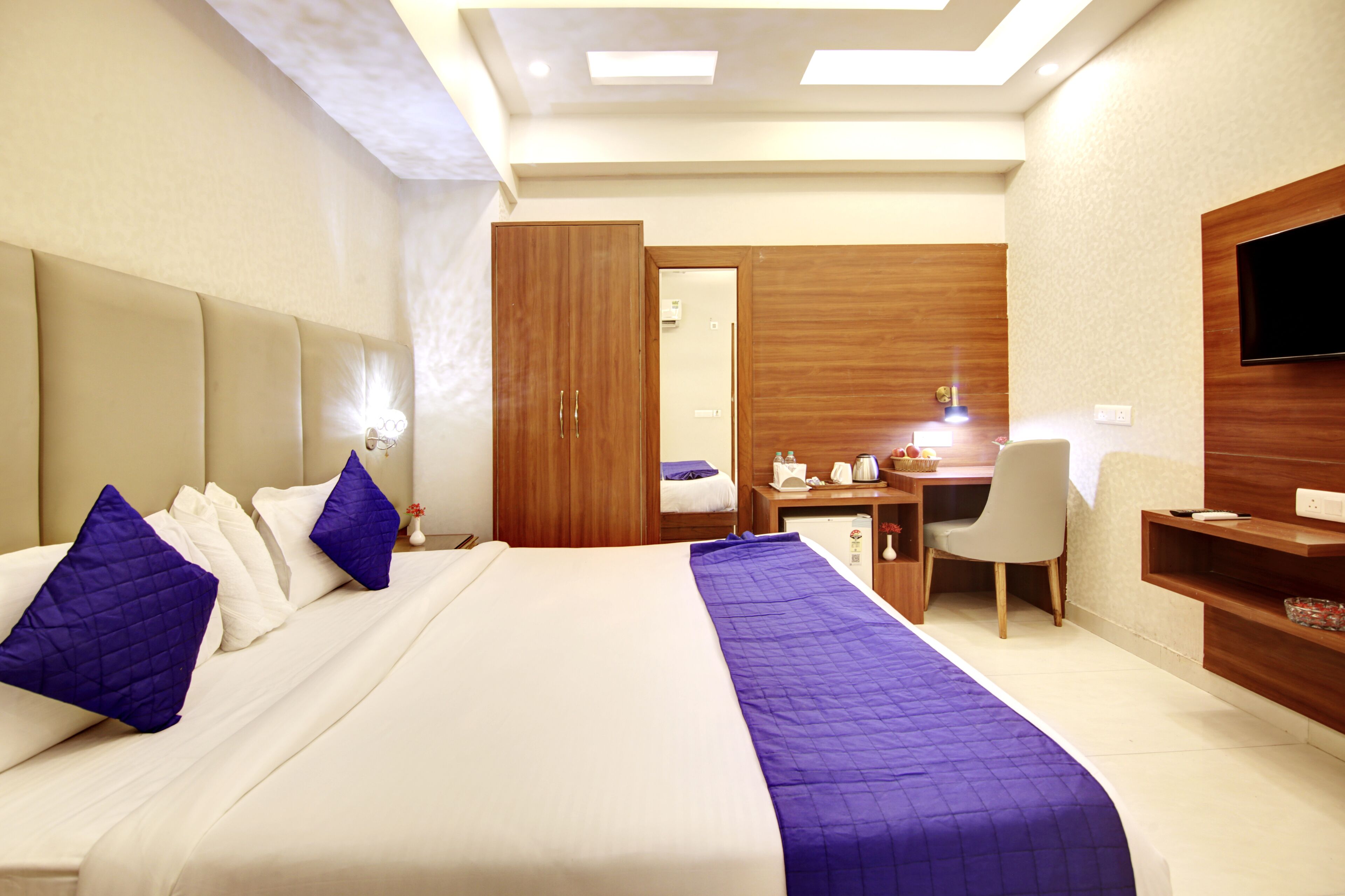 A hotel room with a bed, a desk, a chair, a TV, and a wardrobe.