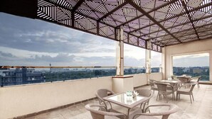 A rooftop terrace with wicker furniture and a patterned ceiling, overlooking a cityscape.
