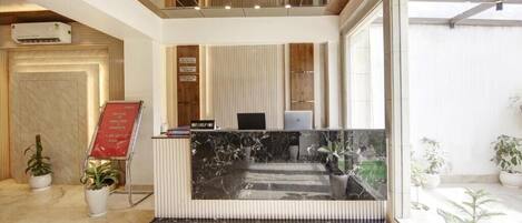 A hotel reception area with a marble counter, potted plants, and a view of the outdoors.