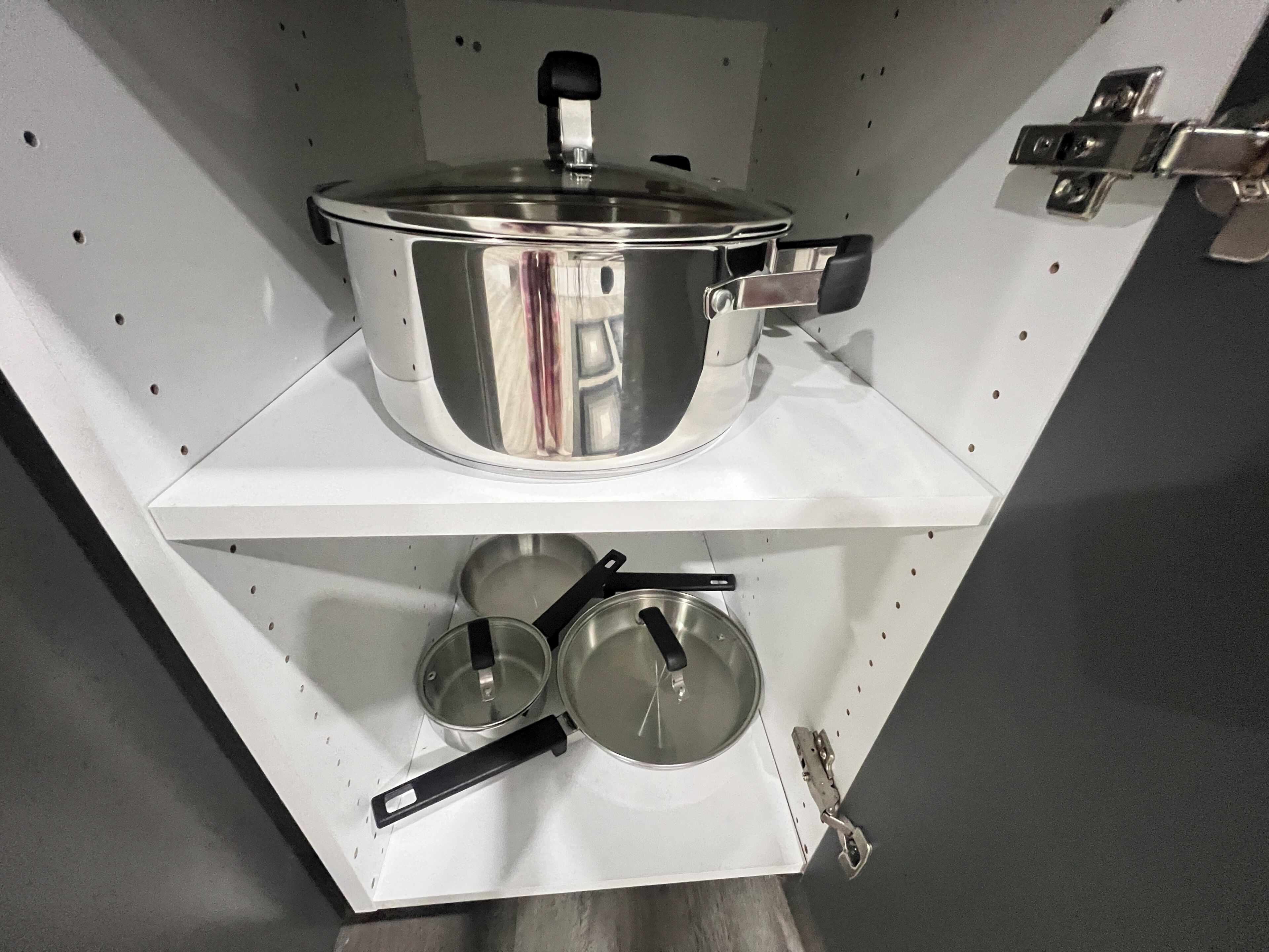 Una cocina con utensilios de acero inoxidable en estantes, incluyendo una olla, sartenes y tapas.
