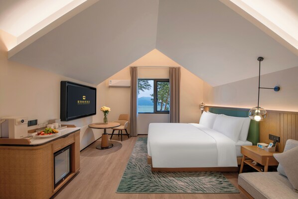A hotel room with a bed, a desk, a TV, a window with a view, and a small table with a vase.