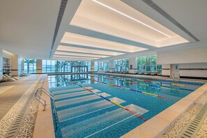 Piscina interna com pistas demarcadas, piso ladrilhado e teto com iluminação embutida.