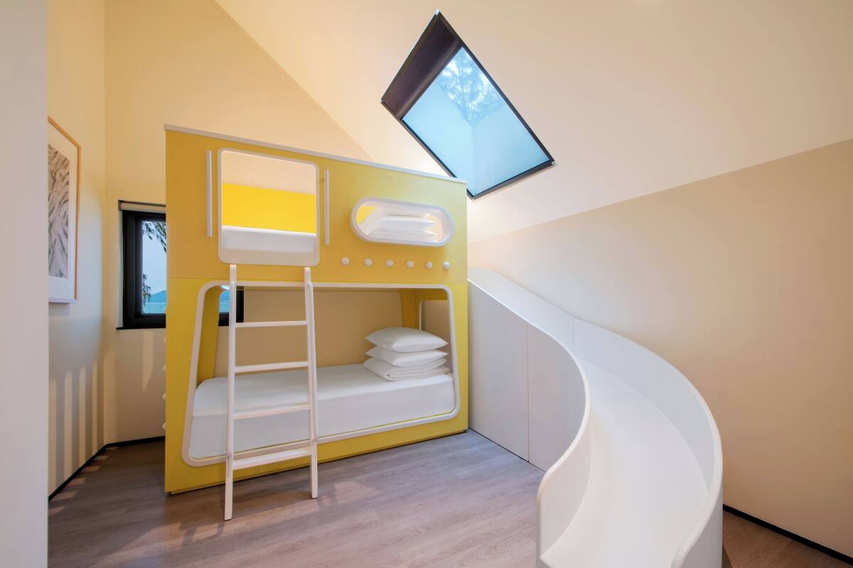 Una cama litera con tragaluz, una escalera espiral blanca y un cuadro en la pared.