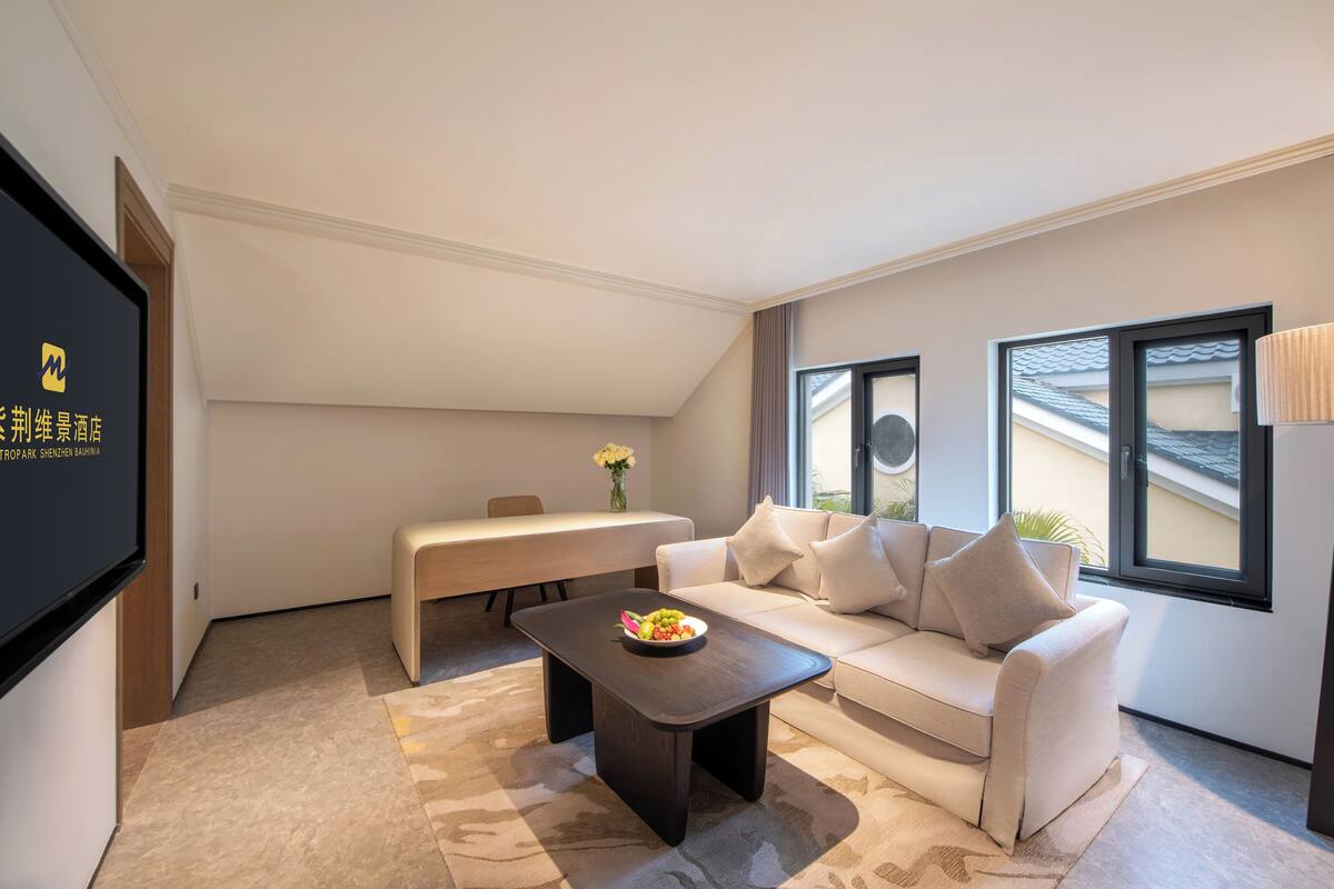 Una habitación de hotel moderna con sofá, mesa de centro, televisor, mesa de comedor y ventana con vistas.