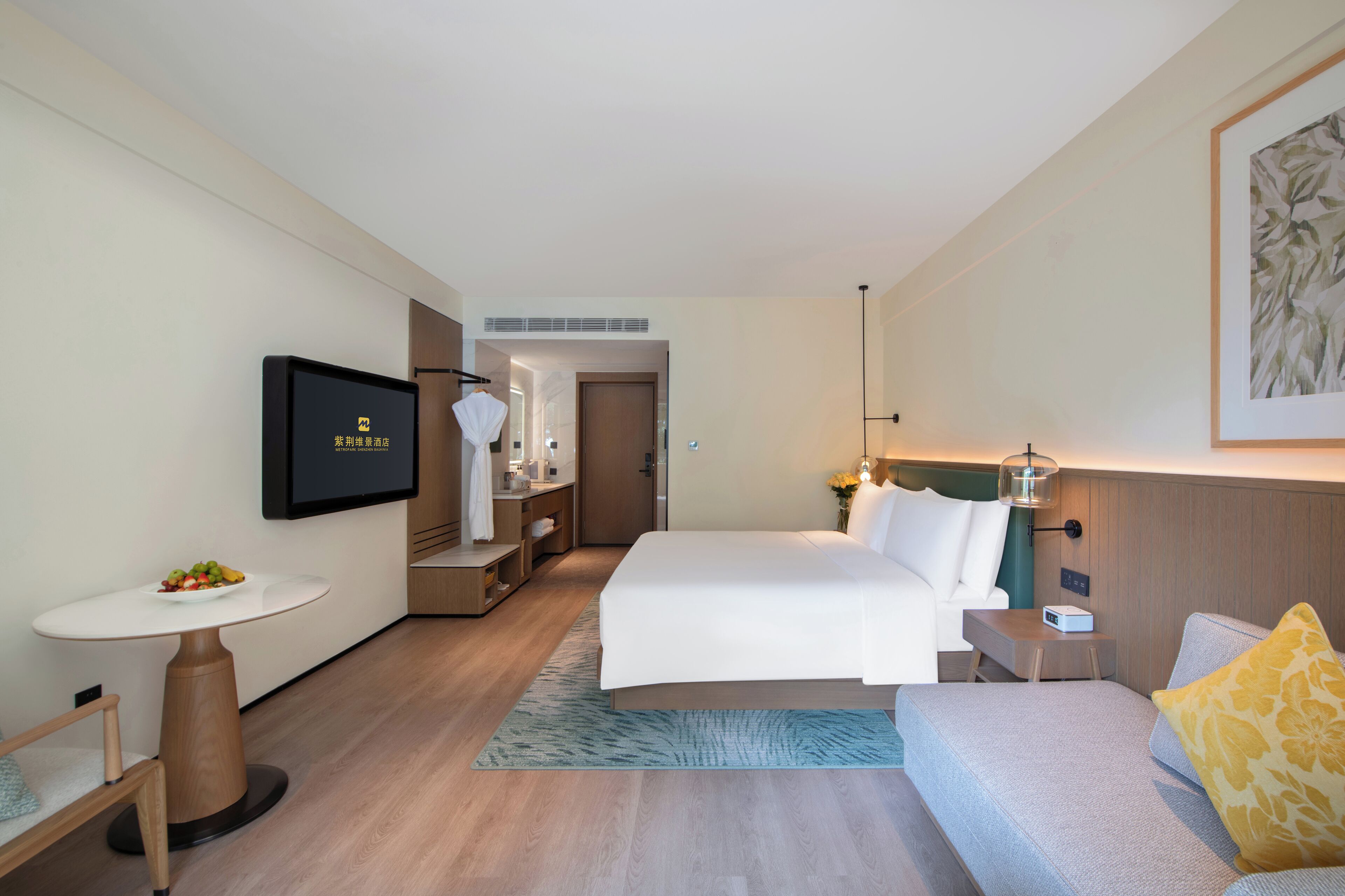 A hotel room with a bed, bedside table, lamp, and a TV on the wall.