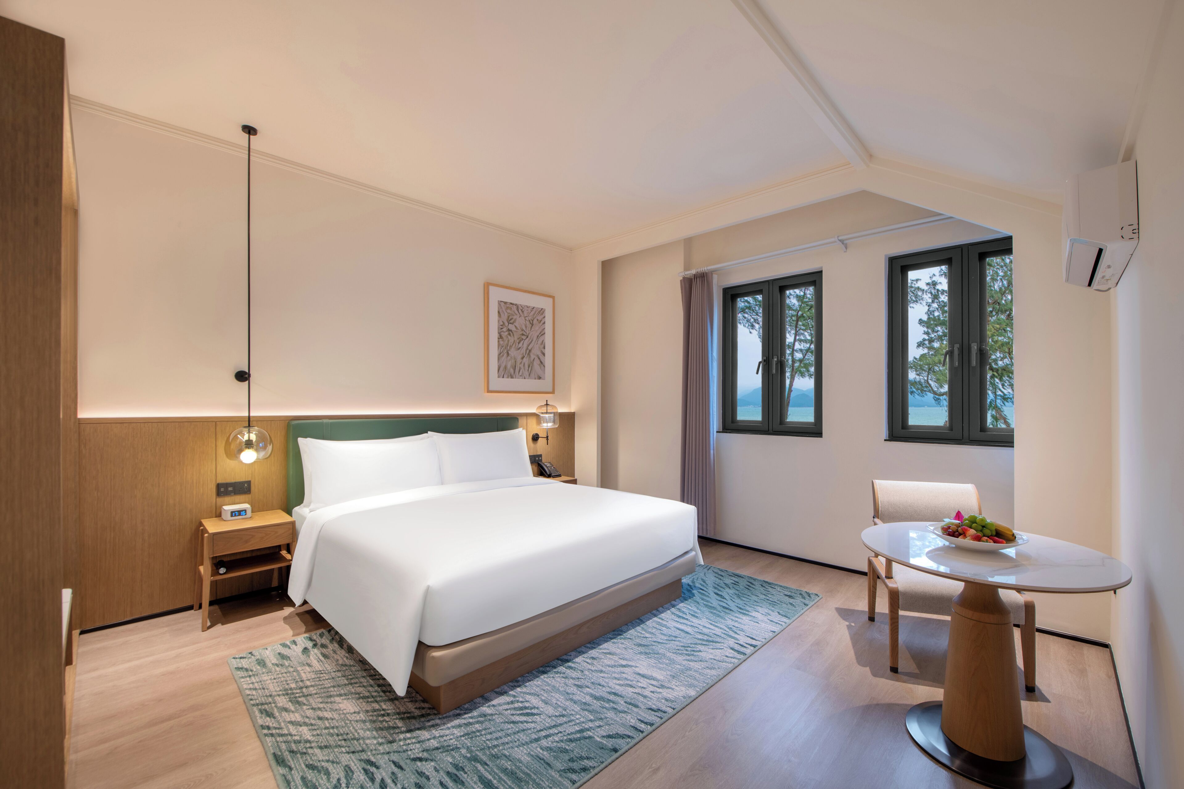 Una habitación de hotel moderna con una cama grande, mesitas de noche, lámpara y una zona de comedor con mesa y sillas.