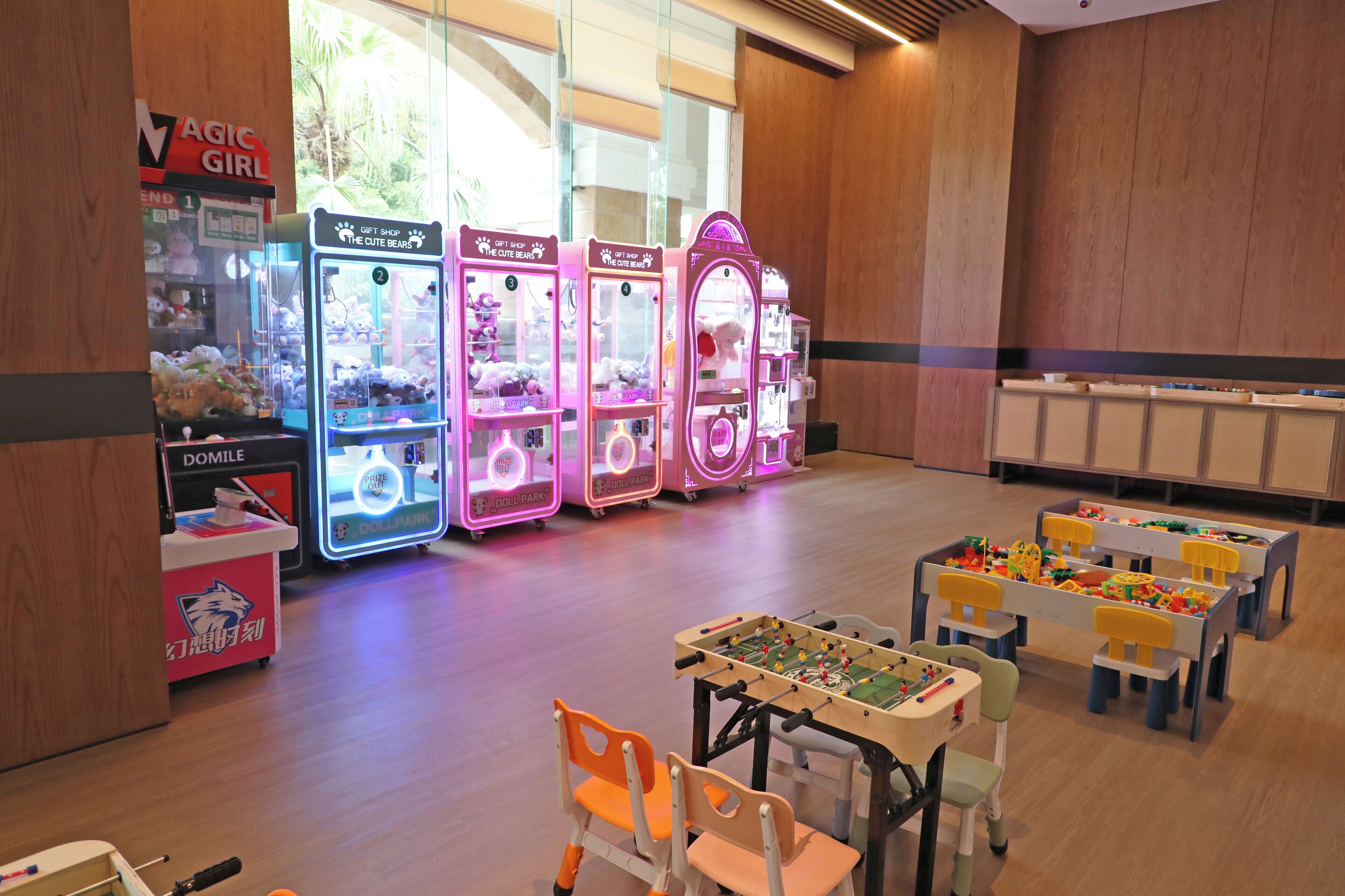 Zona infantil con máquinas de pinche, una mesa de fútbol de mesa y pequeñas mesas con sillas.