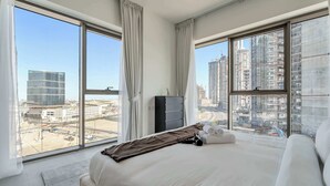 Moderni hotellihuone, jossa on suuret ikkunat, sänky, lipasto ja näkymä kaupungin ylle.